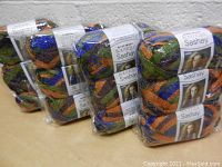 12 skeins of Red Heart Boutique Sashay yarn packaged together showing multi-color ribbon yarn with orange, blue, green and gold.