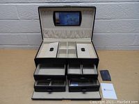 Front view of the open jewelry case displaying mirror, elastic pouch, divided main compartments, and four pull-out drawers.