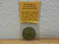 Photo showing the Mexican silver dollar coin encased in plastic with a yellow informational card about José Morelos.