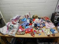 Table covered with assorted vintage doll clothes and accessories including outfits, dresses, and shoes spread loosely and in plastic bags.