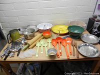 Full view of vintage kitchen items on table showing utensils, baking pans, colander, and other items.