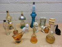 Photo shows 11 vintage Avon bottles in various shapes including cats, birds, lamps, and human figure, some with liquid contents.