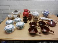 Overview of large assortment of ceramic teapots, canisters, mugs, pitchers, and bowls on table