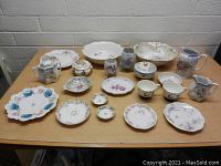 Full view of all 19 vintage porcelain dishes arranged on table showing various sizes and floral decorations with gold accents