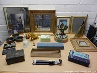 Photo showing wide variety of vintage pictures in frames, mirrors, decorative items including tiger figurine, brass sculpture, glass box, and small tripod.