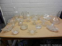 Overview of assorted clear glass items laid on table showing variety of bowls, decanters, dishes, and candle holders with cut glass designs.