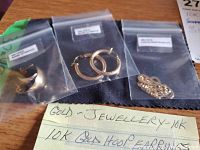 Three resealable bags containing dome earrings, hoop earrings, and necklace with handwritten note listing 10K gold items on wooden surface