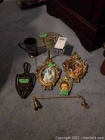 Full lot showing antique iron rest, two decorative brass frames with classical portraits, silver plated cup, brass candle snuffer, and brass stand with unicorn on top.