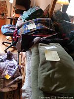 Multiple folded blankets and linens on couch and chairs, including a plaid blanket, green fleece, and other blankets of different materials and colors.