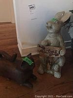 Photo of the bunny figurine holding the 'Welcome' sign and the dark brown cat figurine on the floor.