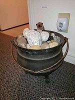 Full view of vintage cast iron cauldron filled with river stones and hedgehog figurine inside