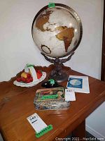 Main display: Atlas-style globe on bronze-tone cast metal stand, white ceramic basket with assorted faux fruit, black stone beaver figurine, rectangular notecard tin
