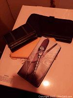 Photo of four items: one pair of black leather gloves and three ladies wallets in various styles including one with a dragonfly design.