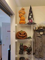 Photo of Halloween decorations on white shelving unit including stacked jack-o'-lantern pumpkins, witch hat, large pumpkin, and figurines.
