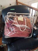 King size bedding set packaged in a clear plastic zippered bag with white braided rope handles, sitting on a chair.