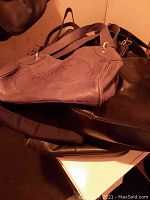 Leather handbags stacked showing a brown Prada Milano bag on top and other dark leather bags beneath.