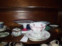 Shelf with assorted glass and porcelain items including Limoges cake plate, floral dishes, and music box.