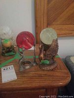 View of both mineral stone globes and their metal stands on a wooden surface, showing size and design contrast.