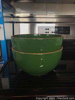 Stacked green ceramic mixing bowls with tan rim, on stove.