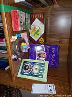 Photo of all items together on wooden surface including the books, Tarot deck, I Ching cards box, and cat rune figurines in wooden bowl.