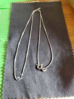 Silver box link chain necklace laid out on fabric background, showing clasp and chain design.