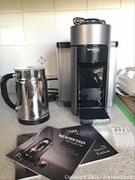 Nespresso VertuoLine Evoluo coffee machine with accompanying milk frother and user manuals, shown on kitchen counter.