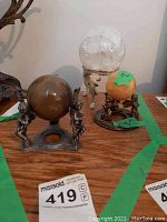 Photo showing three metal stands each with a different onyx ball (brown, clear, orange) arranged on a wooden surface with pricing labels.