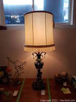 Front view of vintage table lamp lit, showing fabric lamp shade with fringe trim and hanging crystal pendants.