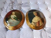 Pair of antique convex portraits lying on quilted surface, showing full frames and painted images
