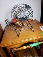 Vintage metal wire bingo cage on a small wooden table. Cage contains colored wooden balls.