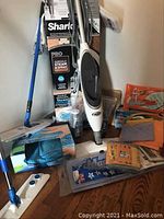 Photo showing Shark steamer and mop boxed unit, microfiber mop pads, various cleaning cloths and supplies, handheld Dustbuster vacuum hose attachment.