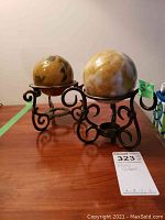 Two stone globes displayed on black metal stands on a wooden surface. Each globe is polished with marbled yellow and cream coloring.