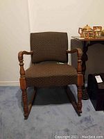 Front view of the vintage rocking chair showing dark brown fabric with small dotted pattern and wooden armrests and legs.
