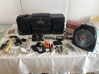 Overview of lot items on table with JVC boombox, Vornado fan, Belkin router in box, tools, lighting, and assorted electronics.