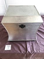 Front angled view of a silver painted wood storage box with a black latch and fabric interior.
