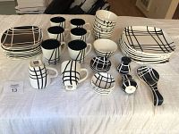Full set of black and white dinnerware with stripe pattern including plates, bowls, mugs, salt and pepper shakers, and spoon rest laid out on a white surface.