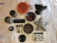 Overview showing all items on white cloth: ceramic candle holders, fossil dish, orange confetti glass bowl, colorful pottery bowls, wax starfish, wooden box with carved soap flower, Art Deco frame, silver spoons, silver earring, and porcelain artwork.