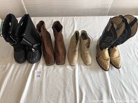 Four pairs of women's boots laid side by side: black snow boots, brown suede low boots, beige low boots, and snakeskin cowboy boots.