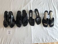 All four pairs of black women's sandals aligned side by side on white cloth background, showing various styles from kitten heel to wedges and slip-ons.