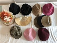 Collection of 11 hats arranged on a white surface including straw visors, fedoras, newsboy and Kangol styles in various colors.