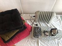 DeLonghi Solaris heater with wool blankets, ironing board, fabric yardage, and sewing supplies displayed on a surface
