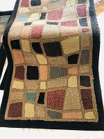 Closeup image of the geometric pattern on one of the rugs showing patchwork squares and rectangles in muted colors on black background.