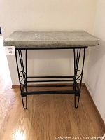 Front view of cement sidewalk cover table with black iron base against a wall.