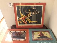 Photo showing three colorful framed and matted prints: a koi fish print with predominantly red and yellow koi on black background with a red mat, and two Bird of Paradise prints with floral designs in red and yellow flowers with decorative mats.