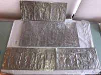 Overview of all four silver-toned metal relief panels laid out on white cloth