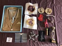 Overall lot contents displayed on brown cloth background including tissue paper suit, printed tortillas, cross stitch, figurines, award, and other items
