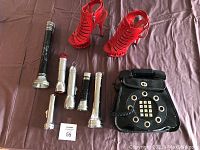 Lot laid out on brown fabric showing red Kotonica high heel sandals, six vintage flashlights, black rotary phone shaped handbag