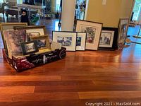 Photo showing an assortment of framed wall art leaning against a wall and placed on the floor, including multiple sizes and frame styles.