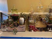 Wide view of the lot showing various glass jars with lids, faux flowers, and some small decorative items in cardboard trays on a table.