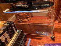 Front-side angle showing clear acrylic construction, two shelves, and caster wheels under the bottom shelf.